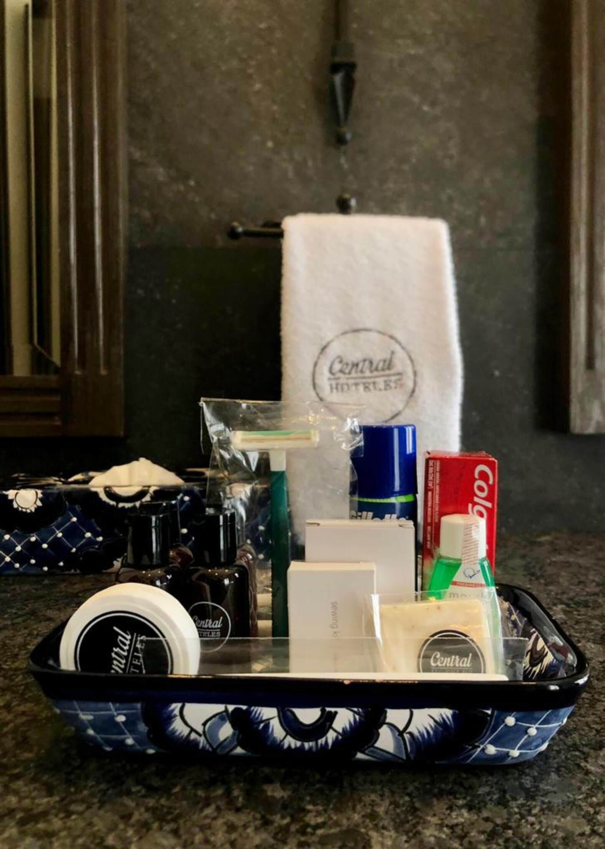 A tray with toiletries including a bottle of Central Hotel's aftershave, a box of Colgate toothpaste, a bottle of mouthwash, and a bar of soap.