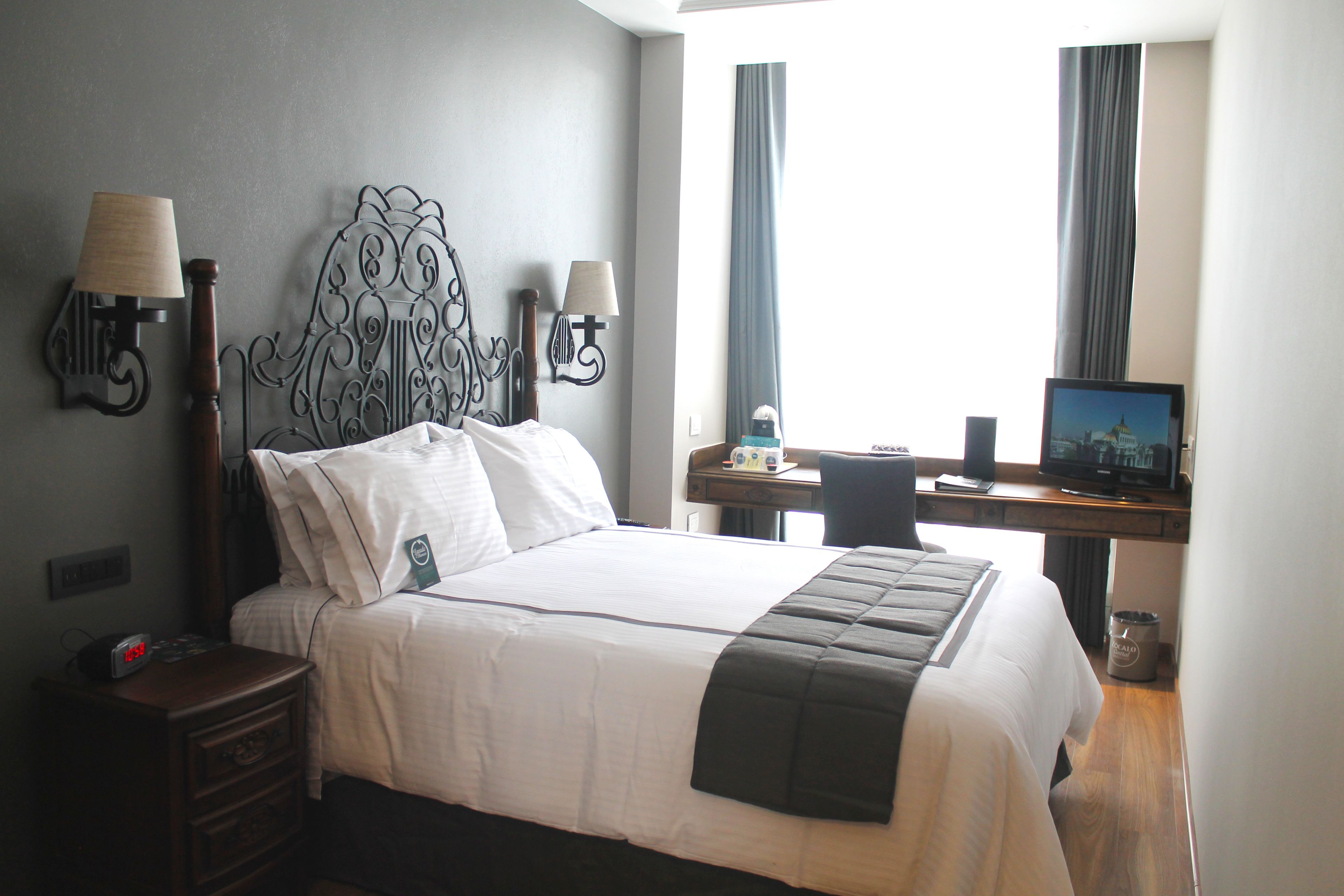 Habitación de hotel con una cama grande, dos lámparas de noche, un escritorio con una computadora y una ventana con cortinas.