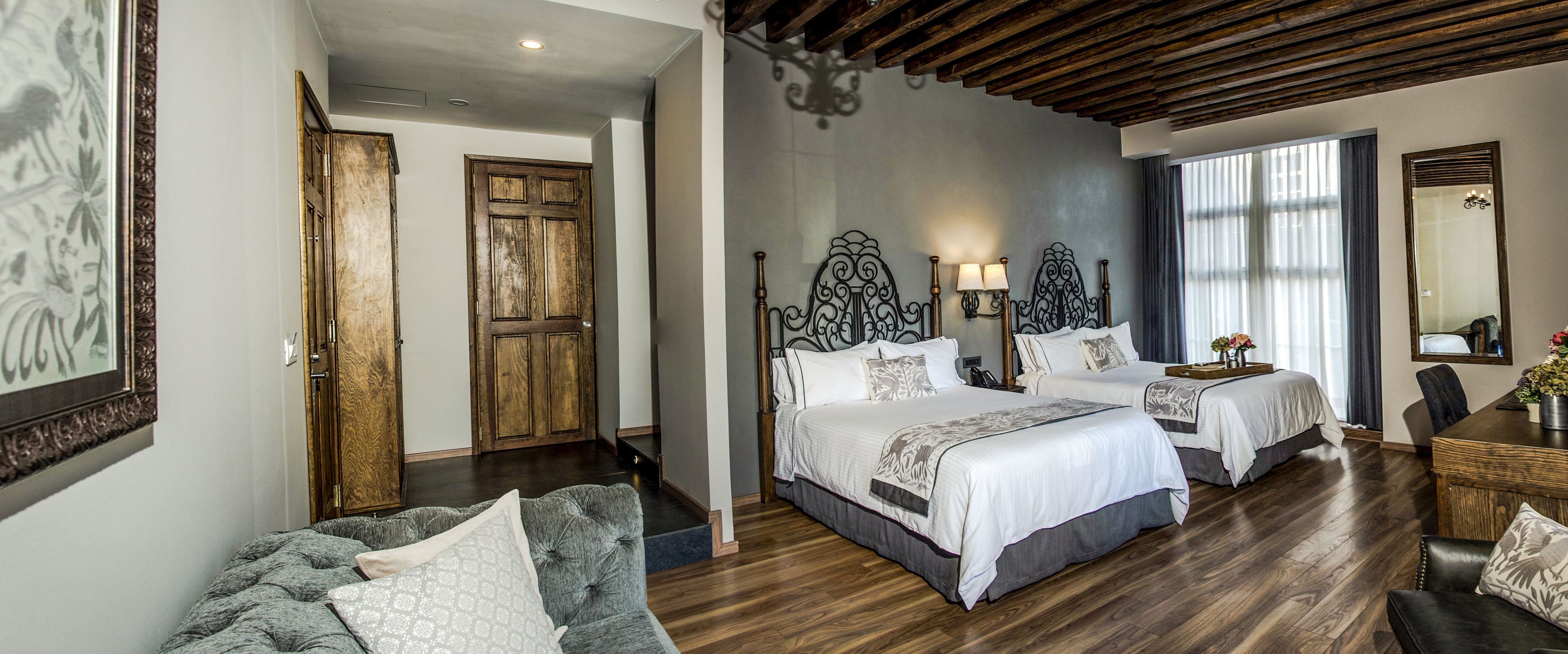 Habitación de hotel con dos camas, techo de madera, un espejo grande y un escritorio con un jarrón de flores.