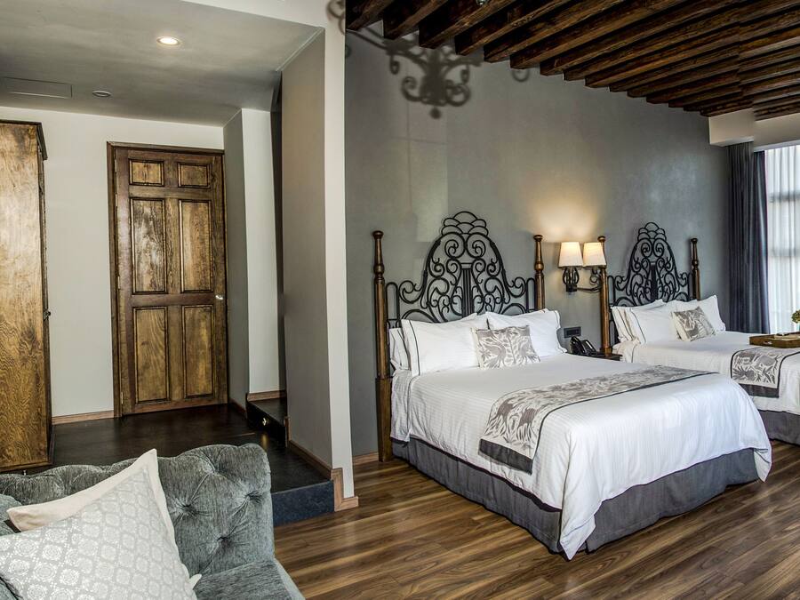 Habitación de hotel con dos camas, techo de madera, un espejo grande y un escritorio con un jarrón de flores.