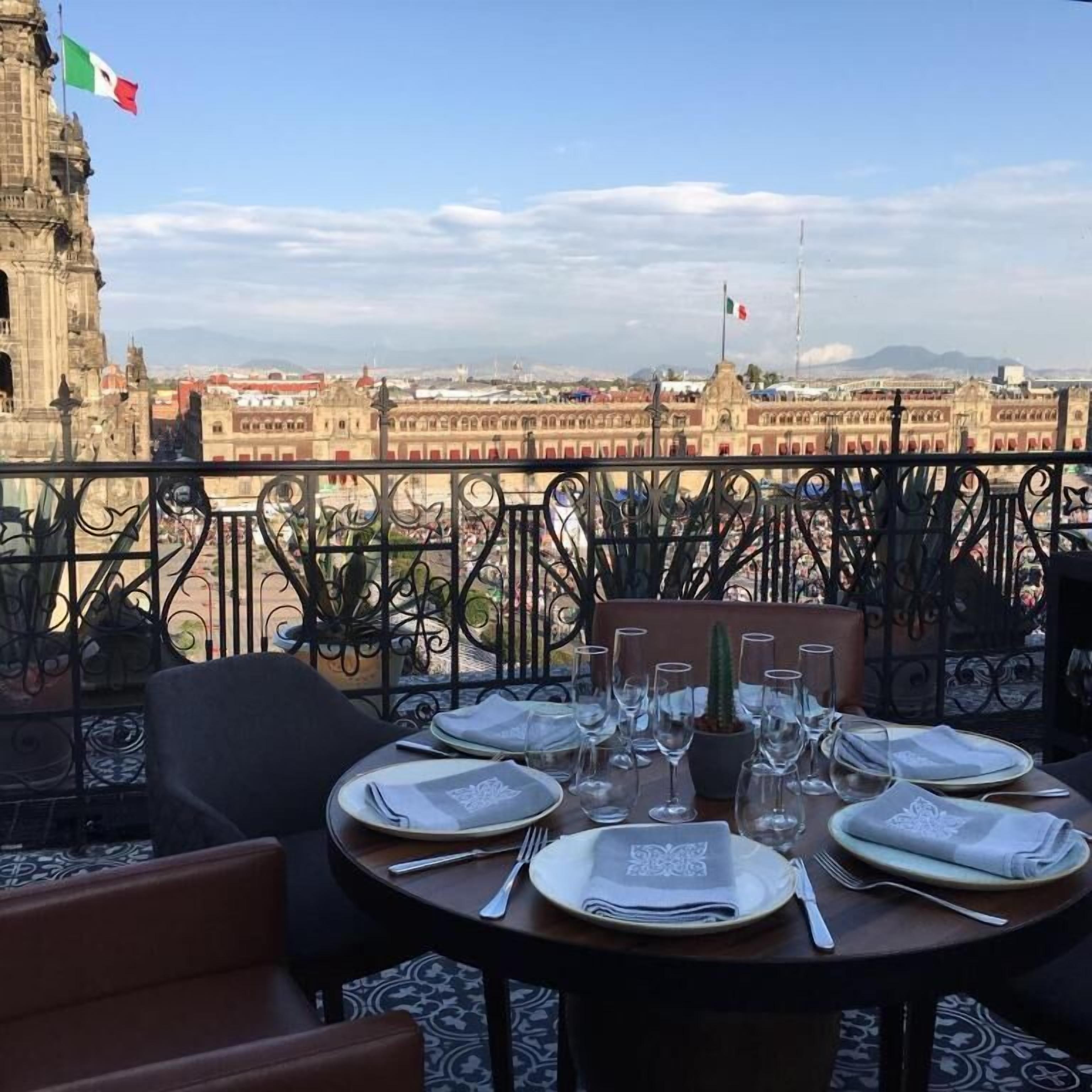 Une table dressée pour le dîner, avec vue sur un paysage urbain, notamment un bâtiment imposant arborant un drapeau.