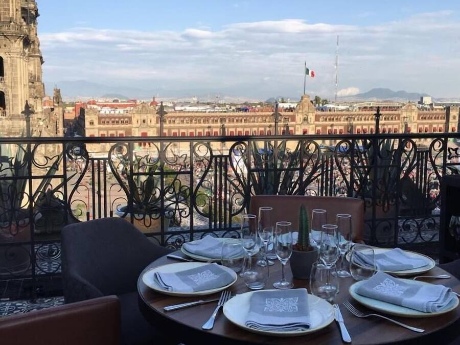 Une table dressée pour le dîner, avec vue sur un paysage urbain, notamment un bâtiment imposant arborant un drapeau.