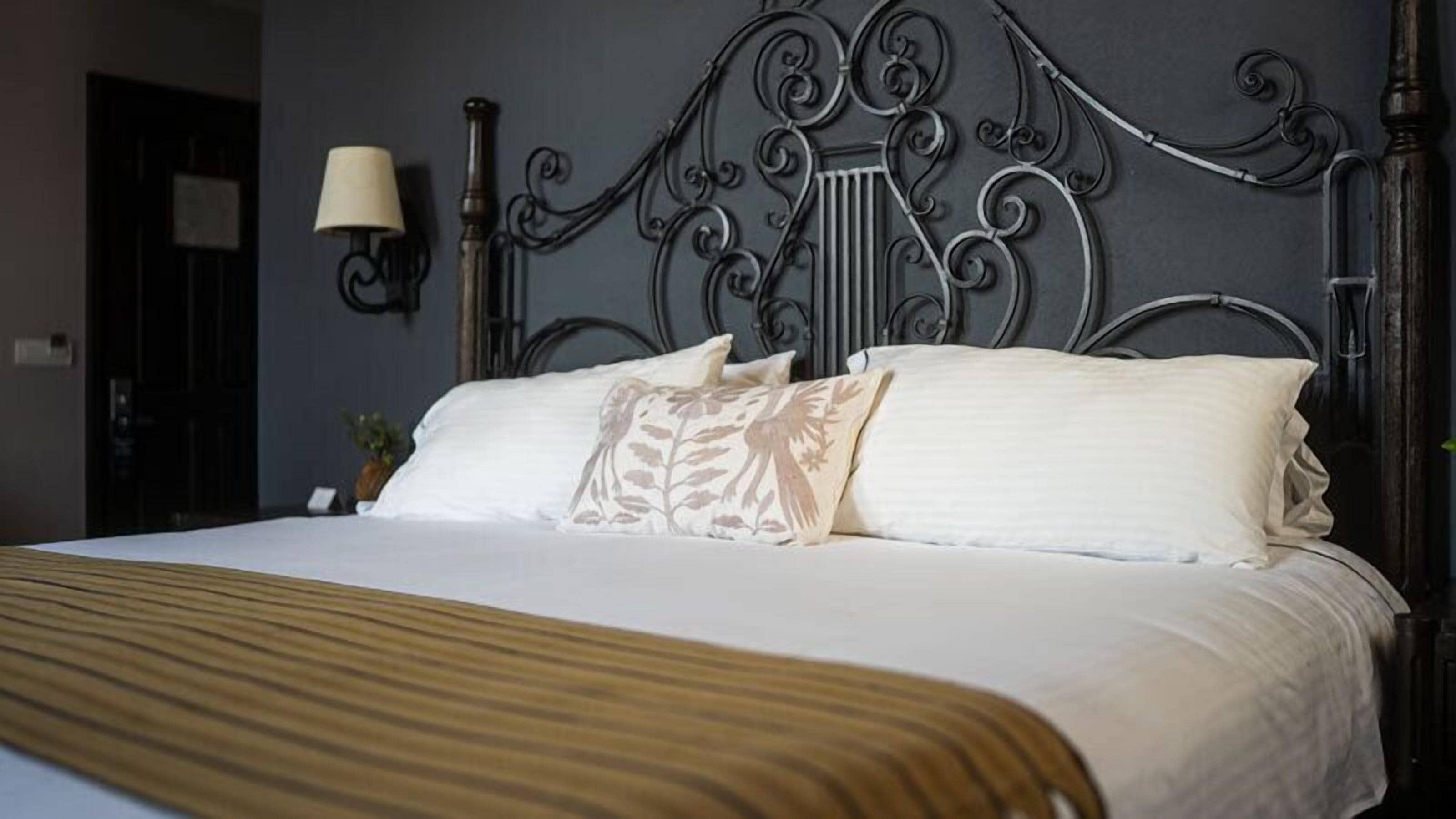 A neatly made bed with a striped bedspread, a decorative headboard, and a wall-mounted lamp.