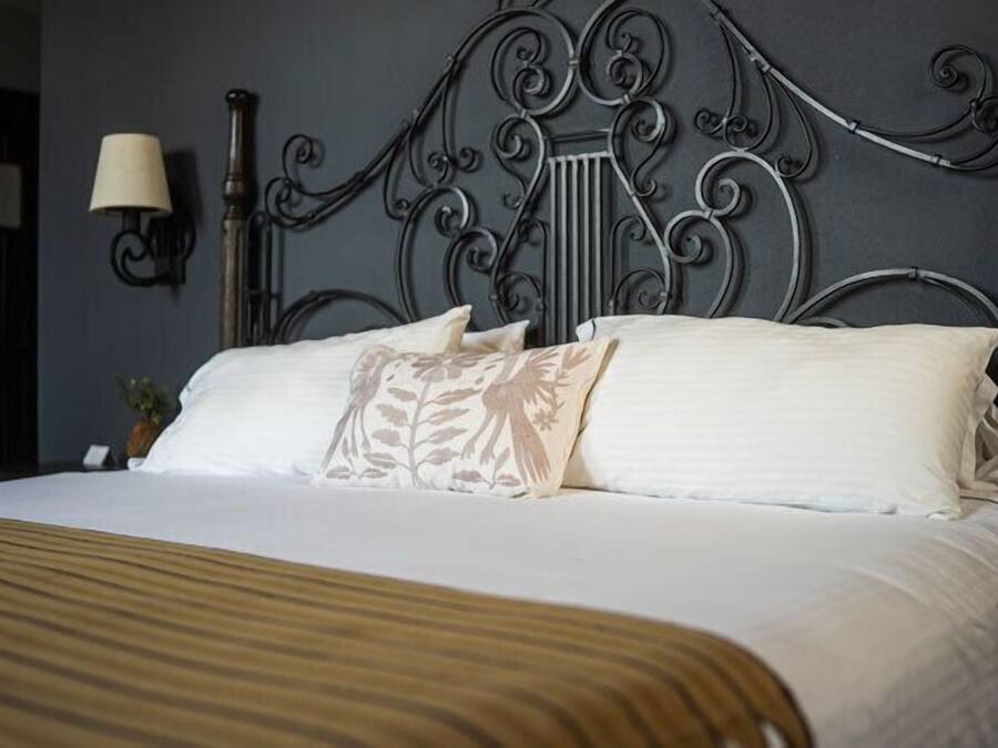 A neatly made bed with a striped bedspread, a decorative headboard, and a wall-mounted lamp.