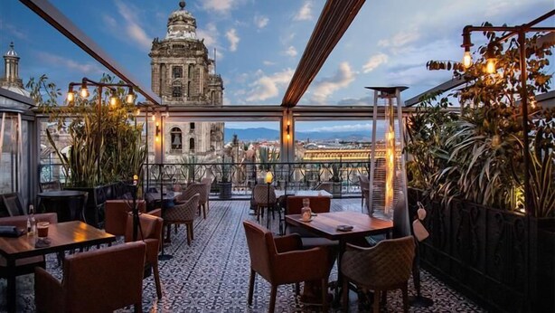 An outdoor dining area with tables and chairs, overlooking a historic building and a bridge.