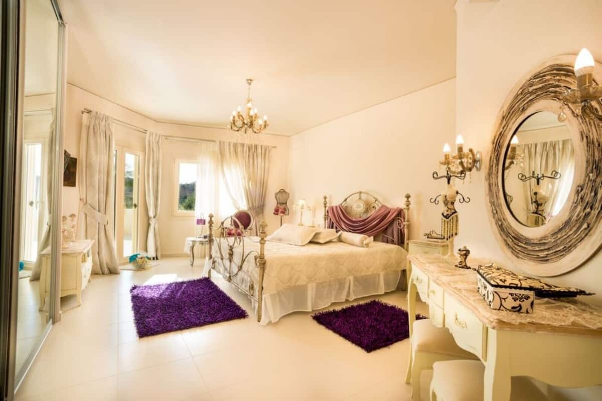 A bedroom with a large bed, a vanity with a mirror, and a chandelier.