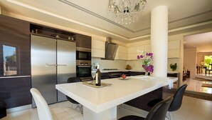 A modern kitchen with a central island, stainless steel appliances, and a chandelier. - Villa Kokalis Resort (Hersonissos)