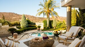 A poolside area with lounge chairs, a woven ottoman, and a view of a mountain. - Villa Kokalis Resort (Hersonissos)
