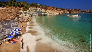 A beach with clear turquoise water, a rocky cliff, and a boat in the distance. - Villa Kokalis Resort (Hersonissos)