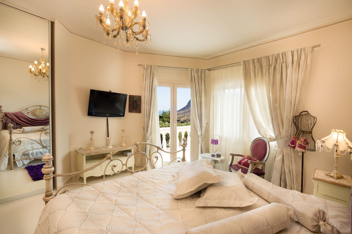A bedroom with a bed, a television, a dresser, a chair, and a view of the outdoors.