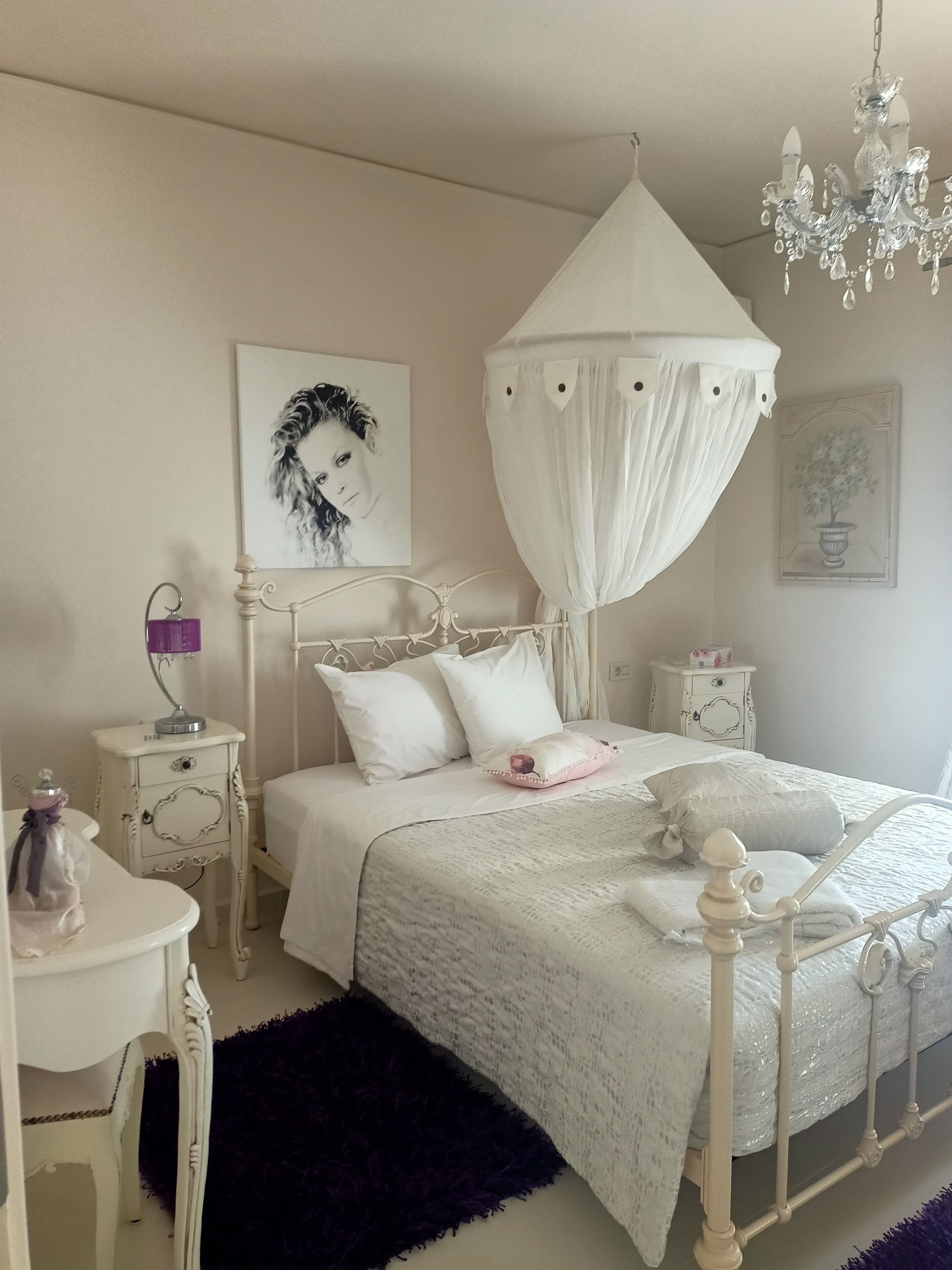 A bedroom with a canopy bed, white furniture, a purple lamp, and a chandelier.