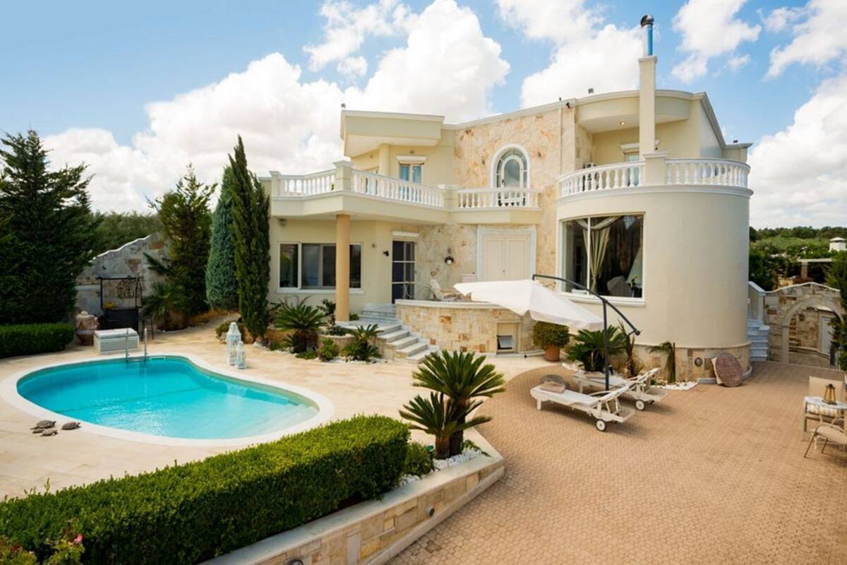 A large, two-story house with a swimming pool, outdoor seating, and a stone facade.