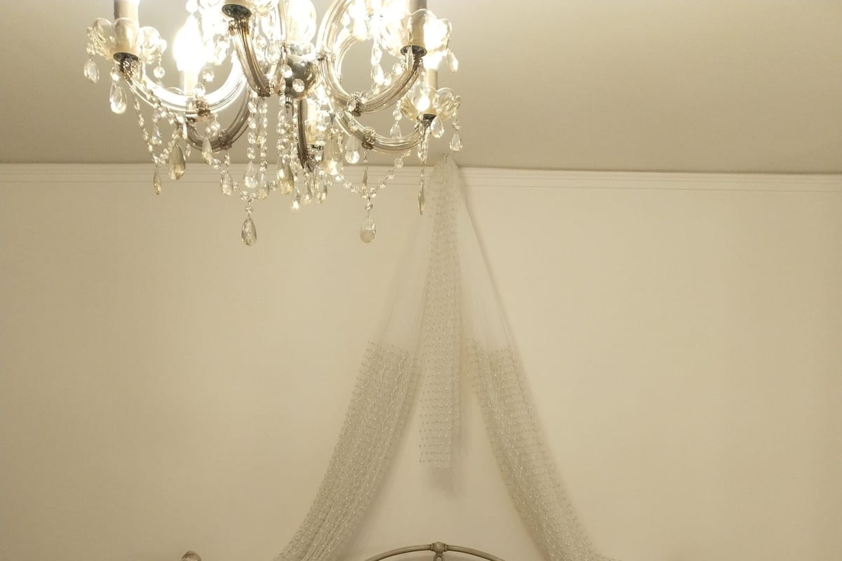 A bedroom with a canopy bed, a chandelier, and a bedside table with a lamp.