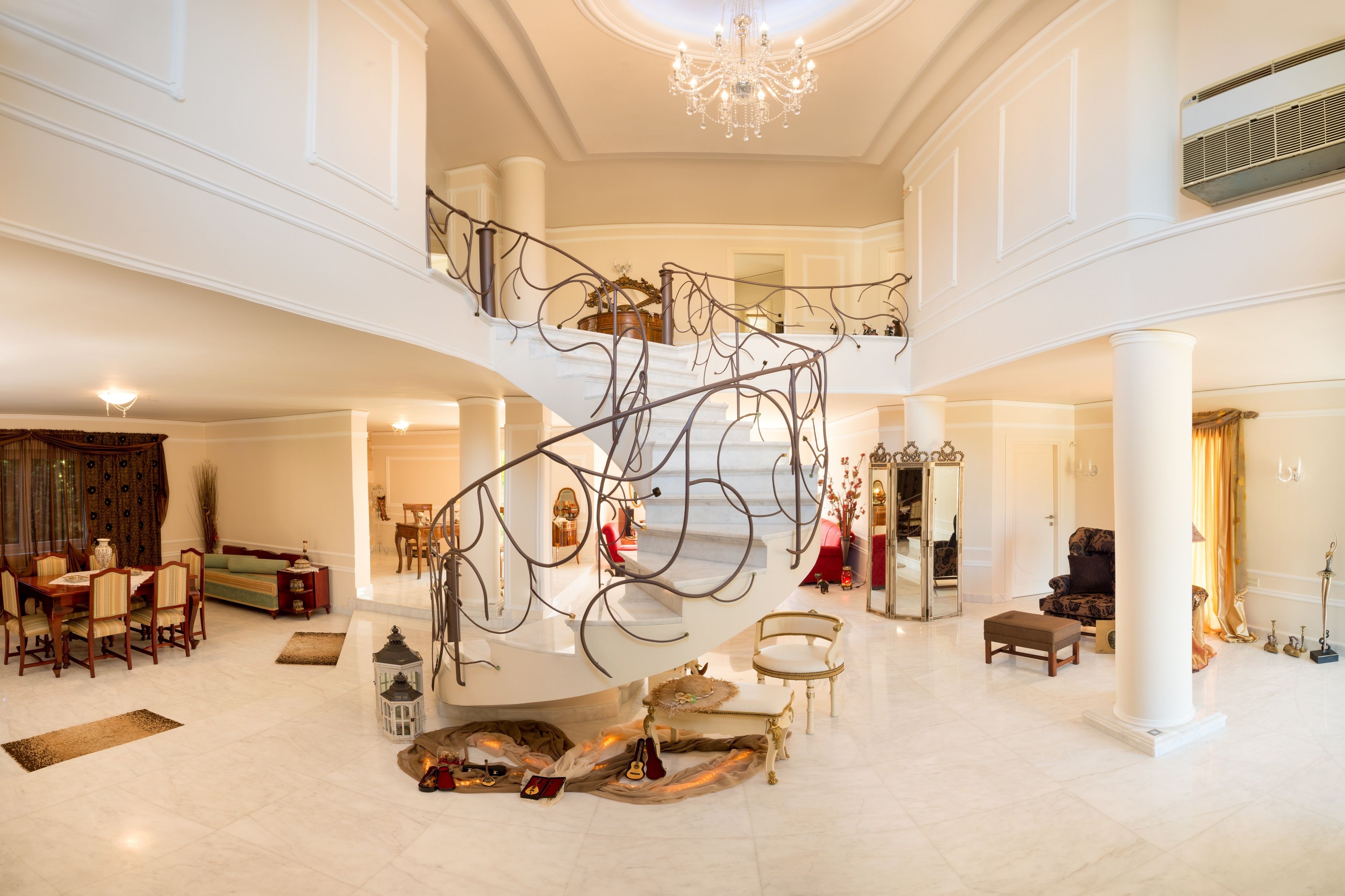 A spacious lobby with a grand staircase, a chandelier, and a high ceiling.