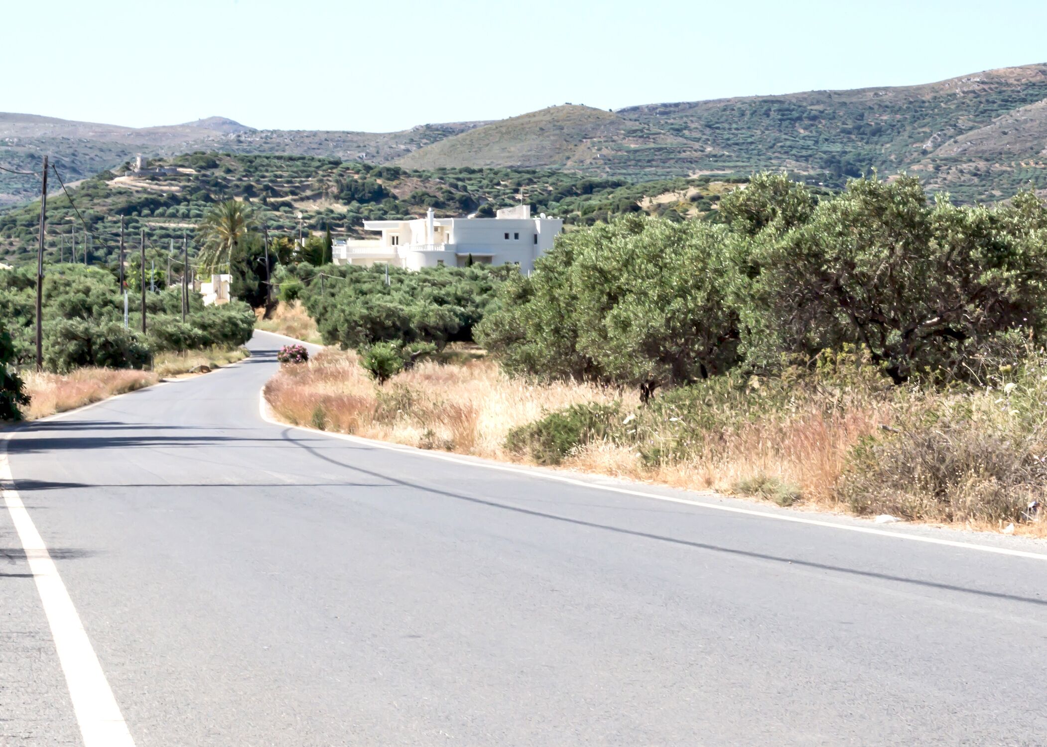 Una carretera serpentea por un paisaje montañoso con vegetación escasa y algunos edificios a lo lejos.