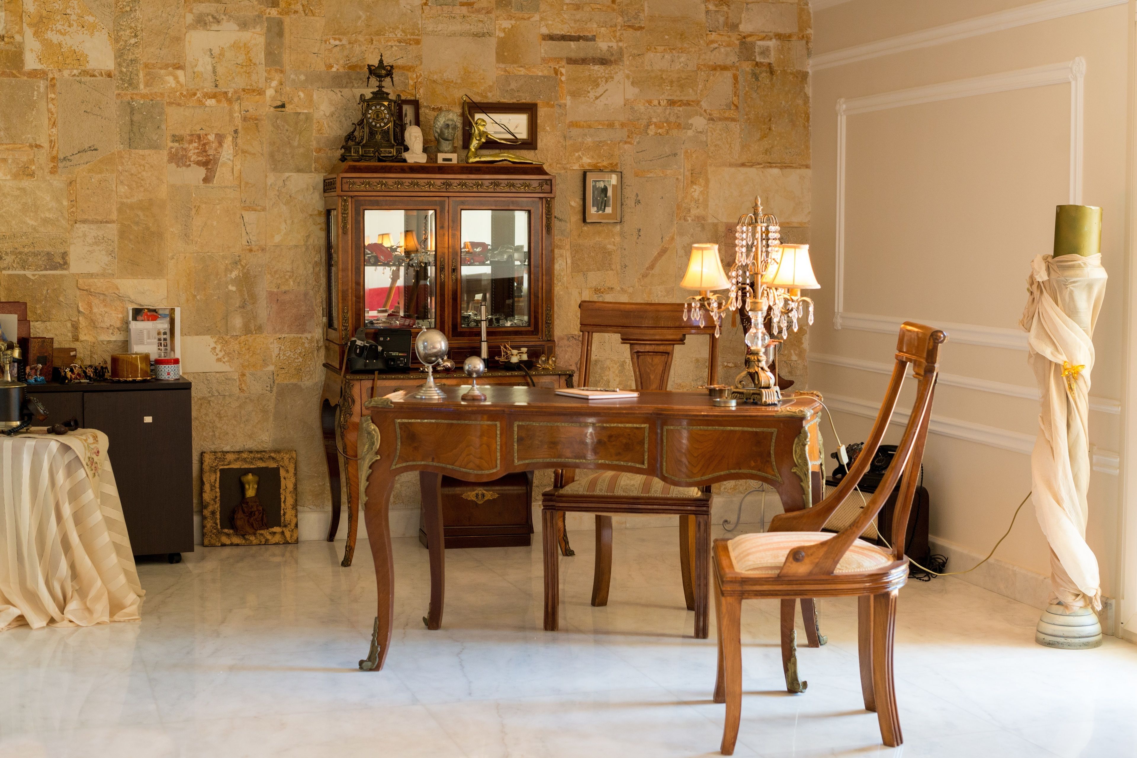 A dining area with a wooden table, chairs, and a chandelier. There is a cabinet with glass doors and a statue on the wall.
