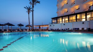 A swimming pool with lounge chairs and umbrellas, a building with balconies, and palm trees. - Sea life Nahariya BY Jacob Hotels (Nahariya)