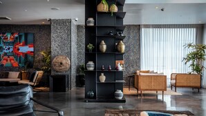 A modern interior with a black shelving unit displaying various decorative items, a seating area with a sofa and chairs, and a large abstract painting on the wall. - Sea life Nahariya BY Jacob Hotels (Nahariya)