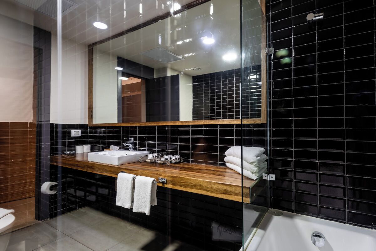 Un baño moderno con tocador de madera, un espejo grande y paredes de azulejos negros.