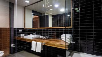 Un baño moderno con tocador de madera, un espejo grande y paredes de azulejos negros.