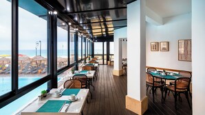A restaurant with outdoor seating overlooking a pool and beach, featuring wooden flooring and modern furniture. - Sea life Nahariya BY Jacob Hotels (Nahariya)