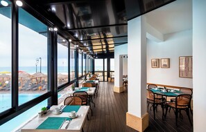 Un restaurant offrant une vue sur la plage et l’océan, doté d’un plancher en bois et d’un mobilier moderne.
