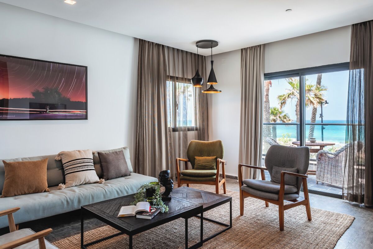 Uma sala de estar moderna com sofá, poltronas, mesa de centro e uma grande janela com vista para o mar.