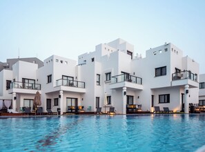 A modern hotel with white exterior walls, balconies with glass railings, and a swimming pool area with lounge chairs. - Sea life Nahariya BY Jacob Hotels (Nahariya)