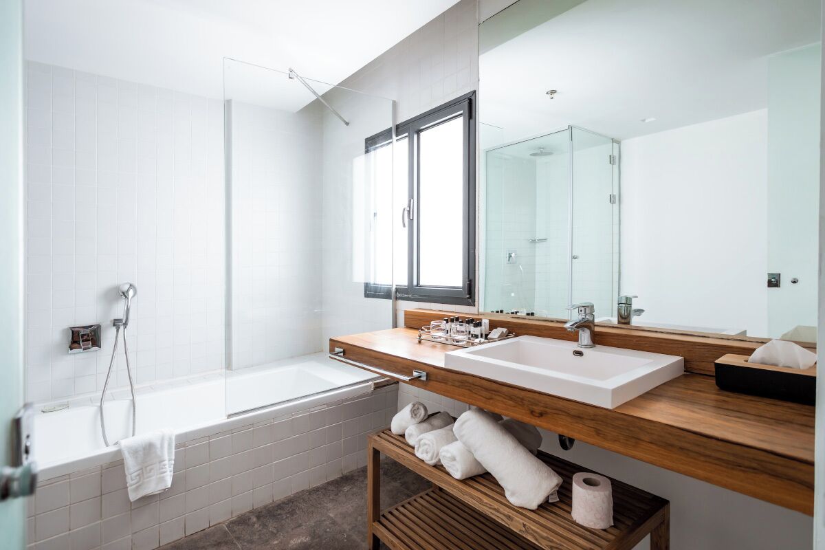 Ein modernes Badezimmer mit einer Badewanne, einem Waschbecken, einem Spiegel und einem hölzernen Ablagebrett mit Handtüchern.
