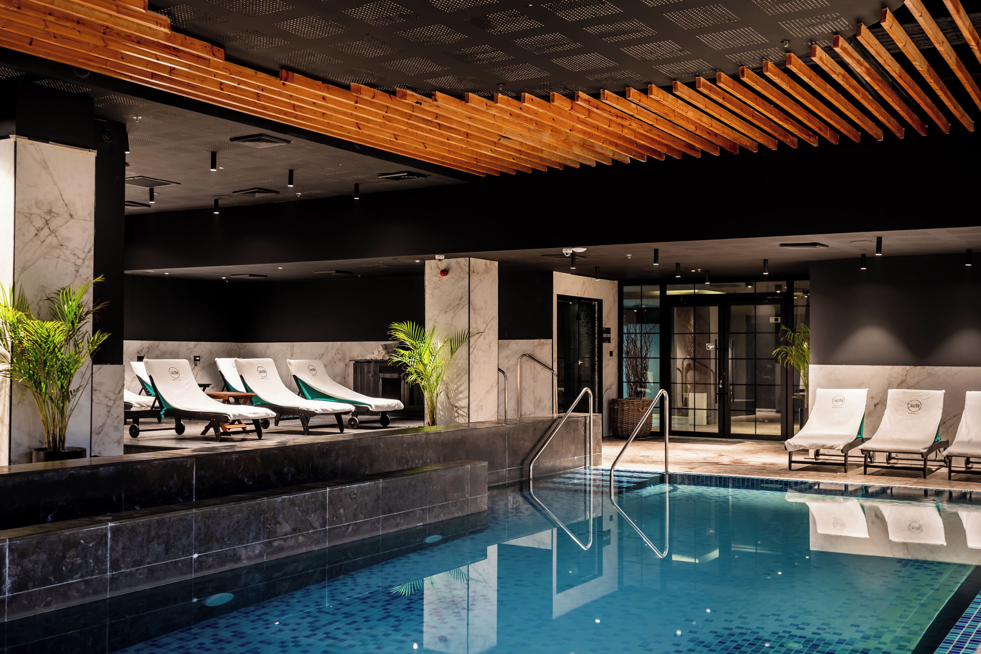 A swimming pool with lounge chairs, a wooden ceiling, and a marble wall.