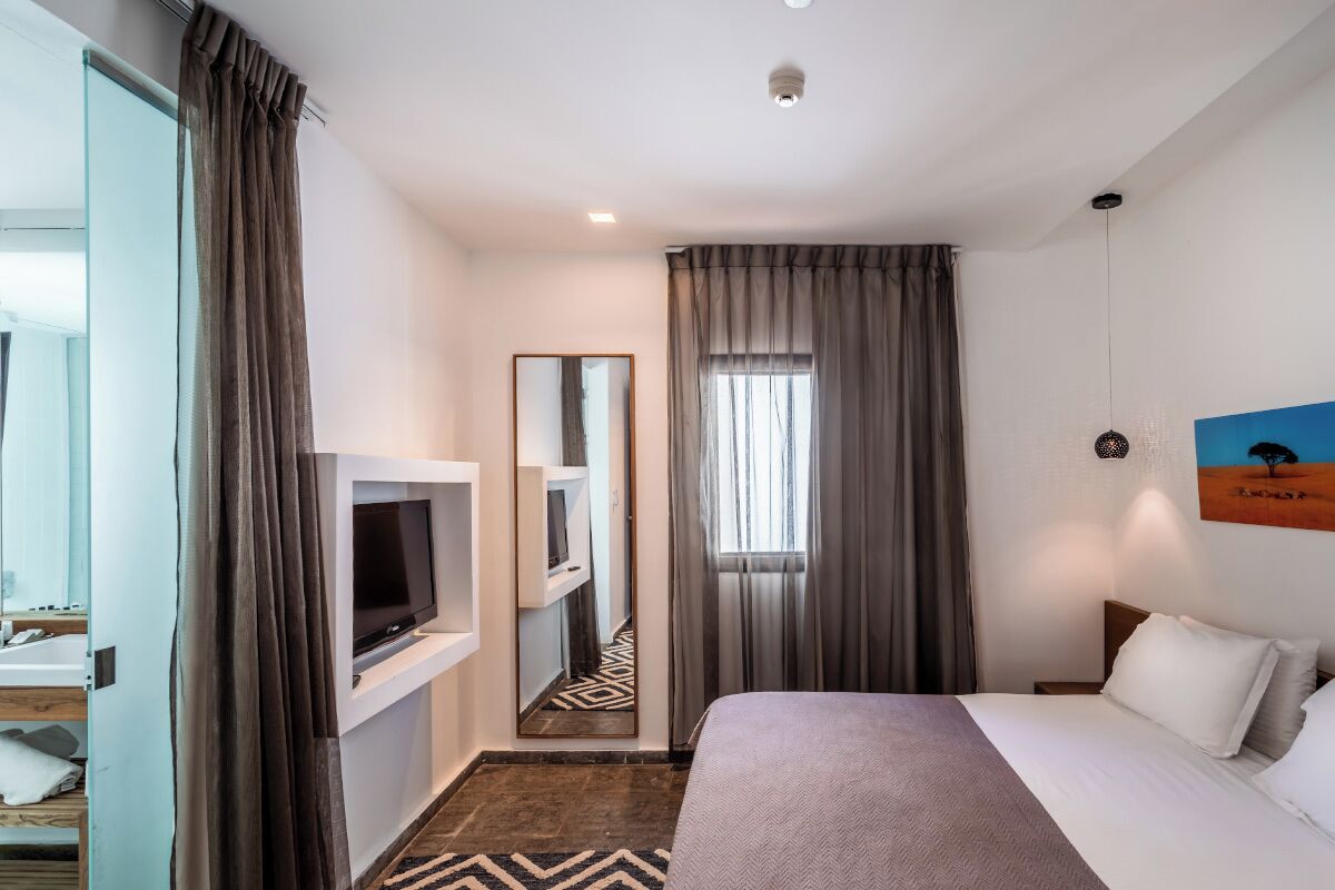 A hotel room with a bed, a TV, a mirror, and a painting on the wall.