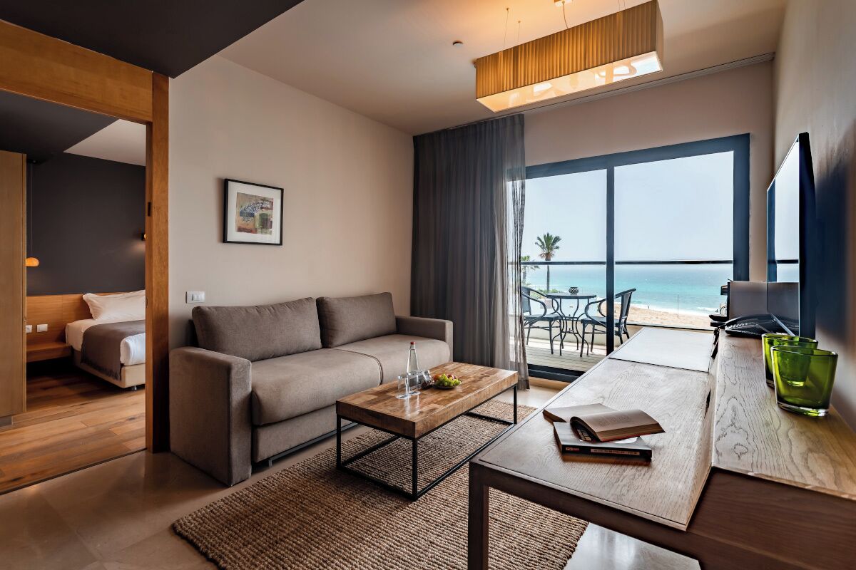 A modern hotel room with a sofa, coffee table, and a view of the beach.