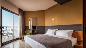A hotel room with a bed, a chair, a table, a mirror, and a balcony. - Sea life Nahariya BY Jacob Hotels (Nahariya)