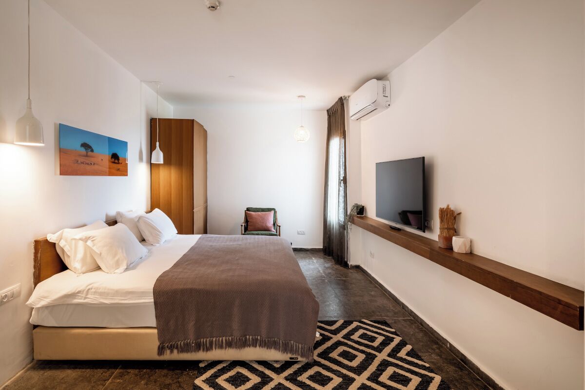A bedroom with a bed, a TV, a chair, and a painting on the wall.