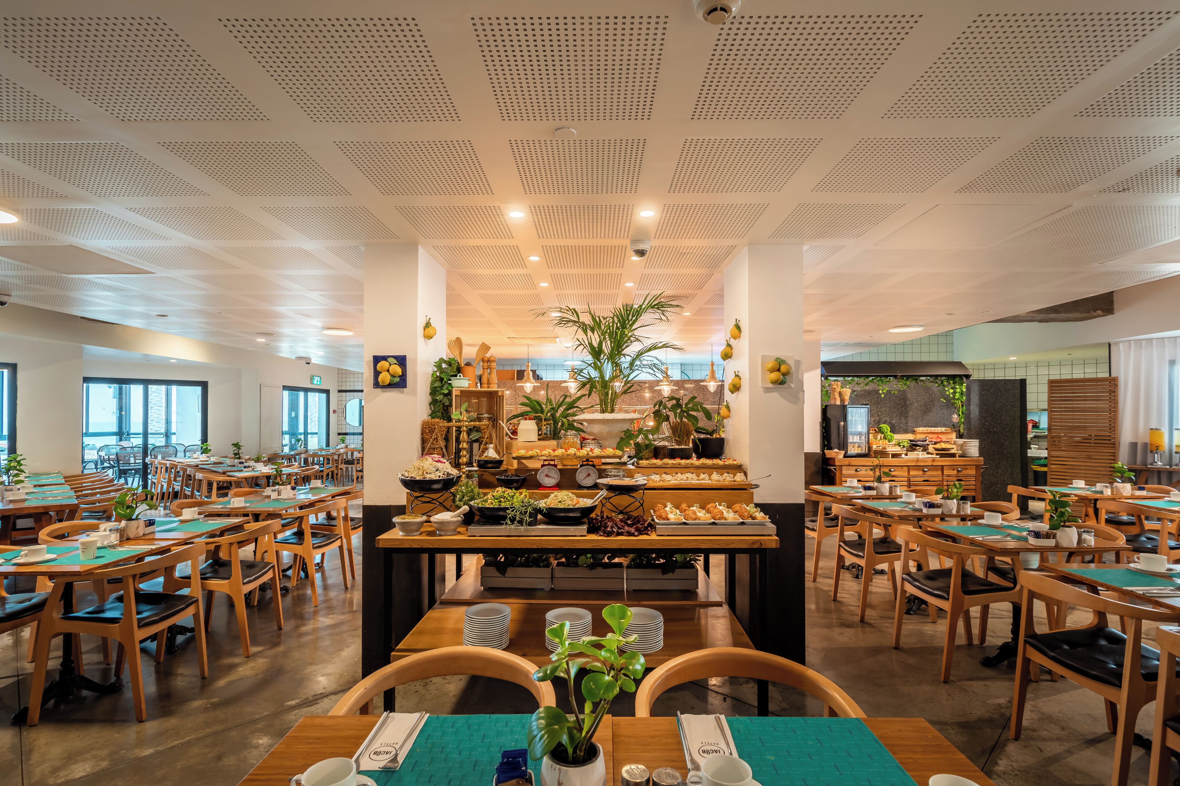 Un'ampia sala da pranzo con diversi tavoli e sedie, un buffet centrale con varie pietanze e piante in vaso.
