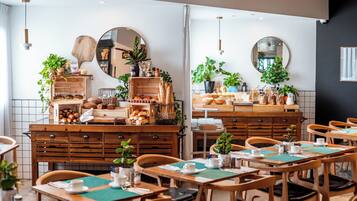 A café with wooden furniture, tables with green placemats, and various baked goods displayed on shelves.