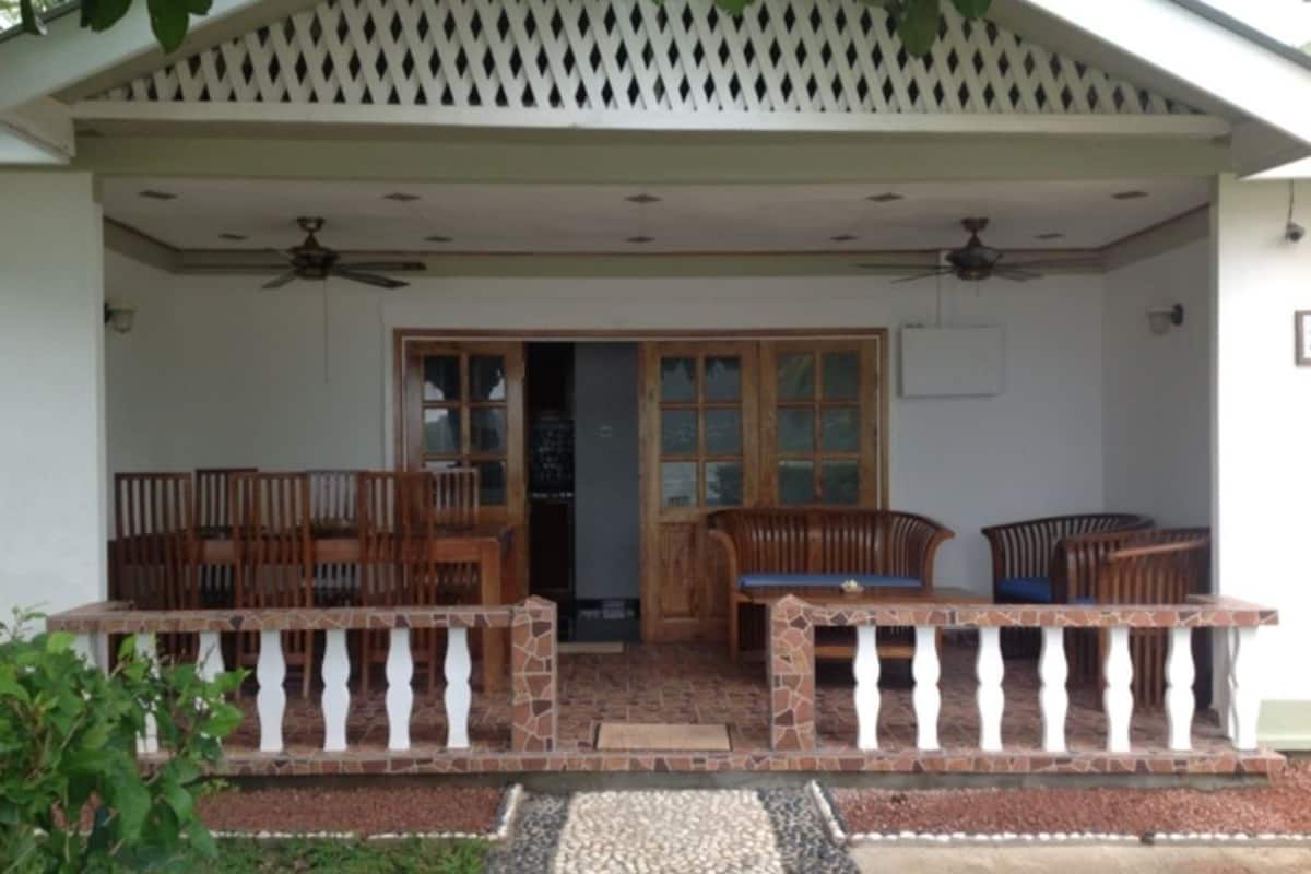 Uma área de estar ao ar livre coberta, com mesa e cadeiras de pátio, um banco de madeira e uma cerca decorativa.