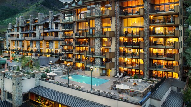 Ein mehrstöckiges Hotel mit Balkonen, einem Pool und einer Bergkulisse.