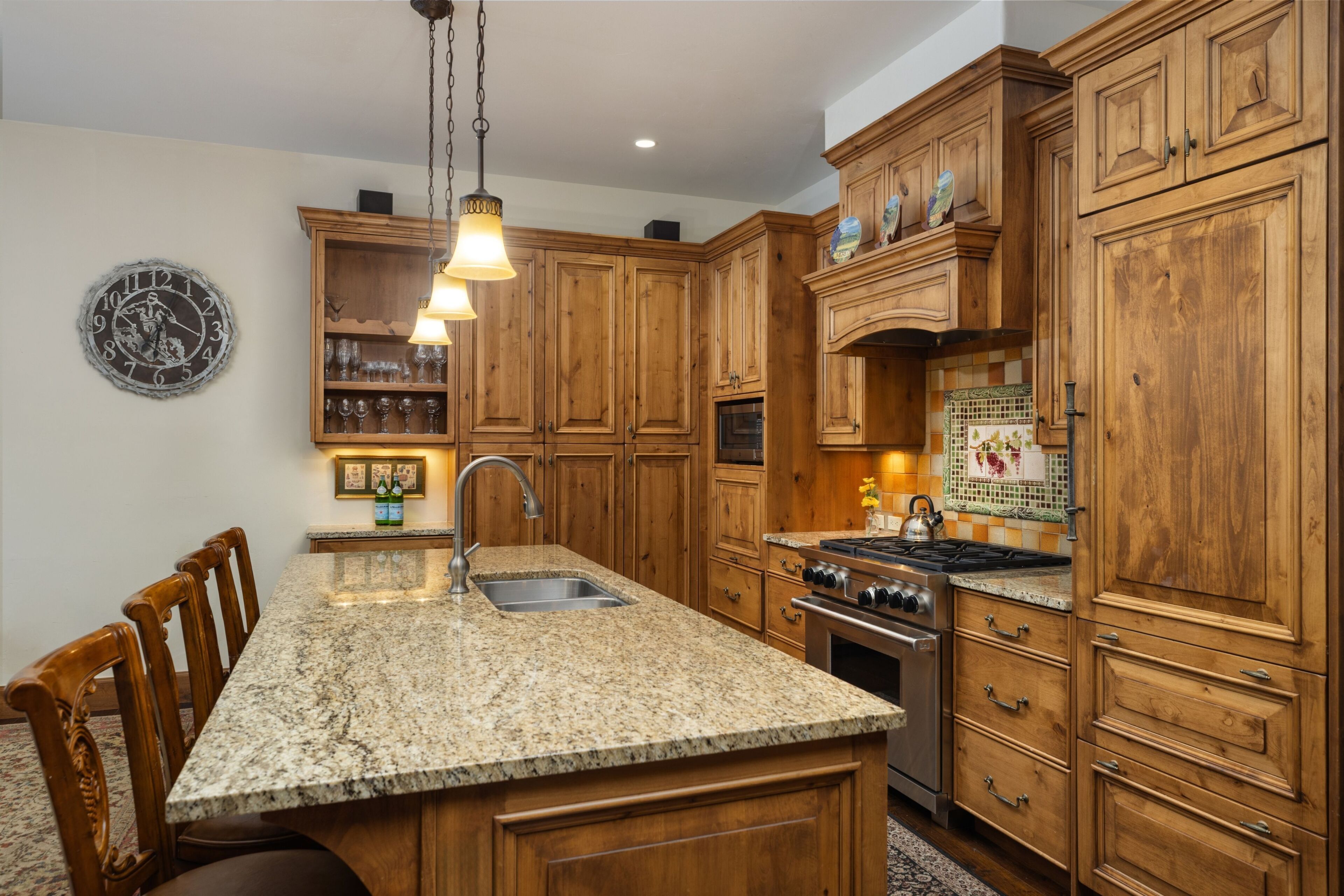 A kitchen with wooden cabinets, granite countertops, a built-in oven, and a hanging light fixture.