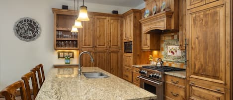 A kitchen with wooden cabinets, granite countertops, a built-in oven, and a hanging light fixture.