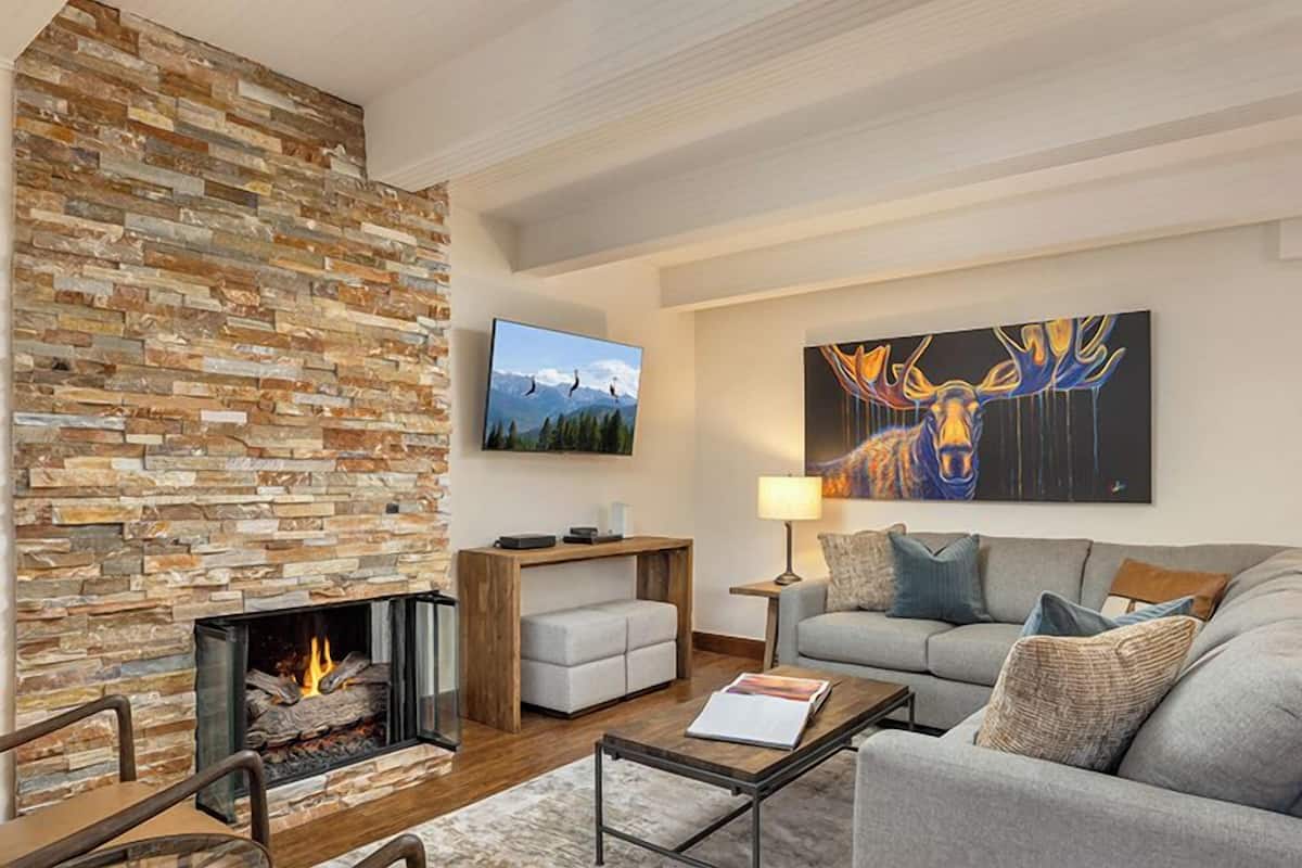 A modern living room with a stone fireplace, a mounted TV, a large abstract painting, and a cozy seating area.