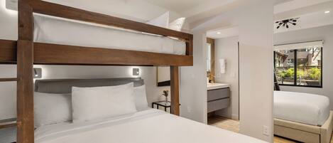 A modern hotel room with a bunk bed, a small bedside table with a vase, and a view of the garden through a window.