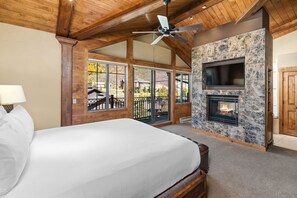 A bedroom with a large bed, a fireplace, a ceiling fan, and a view of the outdoors through large windows. - The Landmark (Vail)