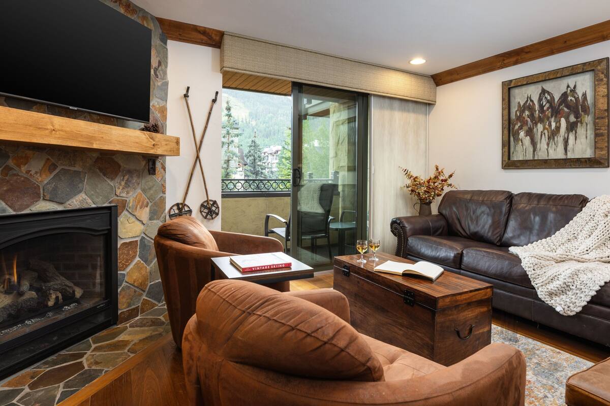 A cozy living room with a stone fireplace, leather sofa, and a large painting.