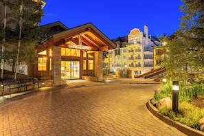 A hotel entrance with a sign reading 'The Landmark,' paved walkway, and surrounding buildings. - The Landmark (Vail)
