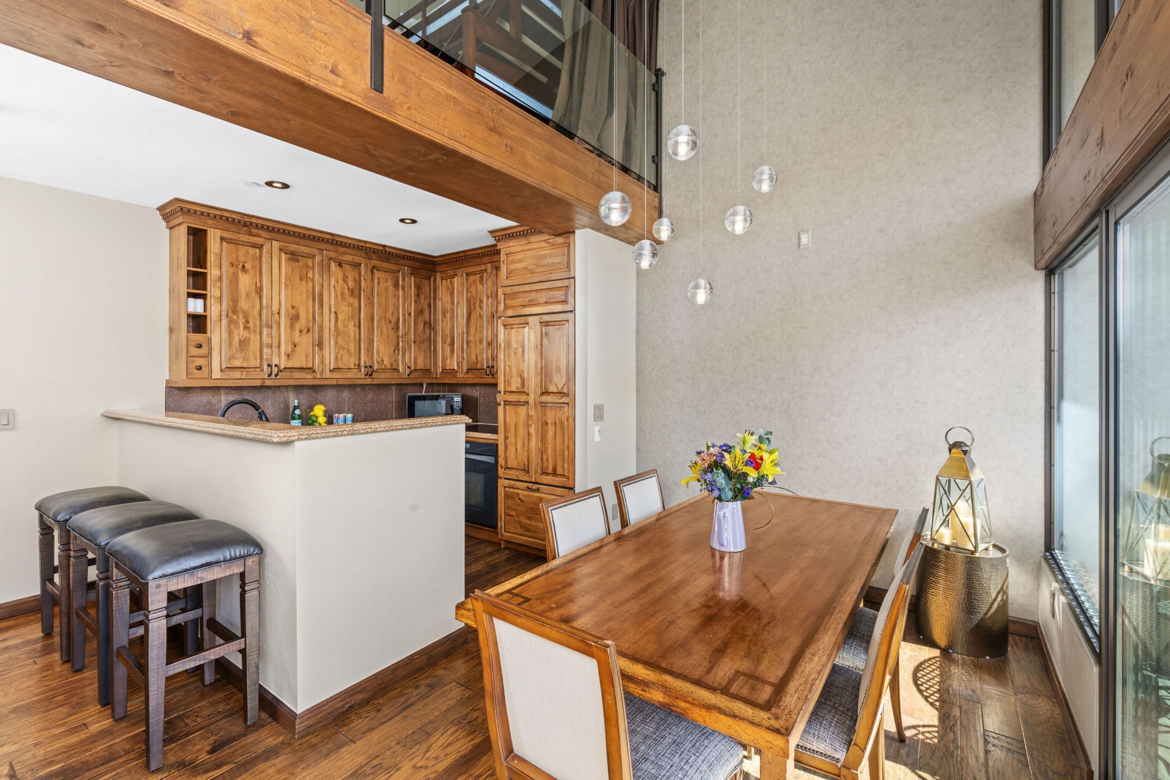 A modern kitchen with wooden cabinets, a dining table with chairs, and a small island with stools.