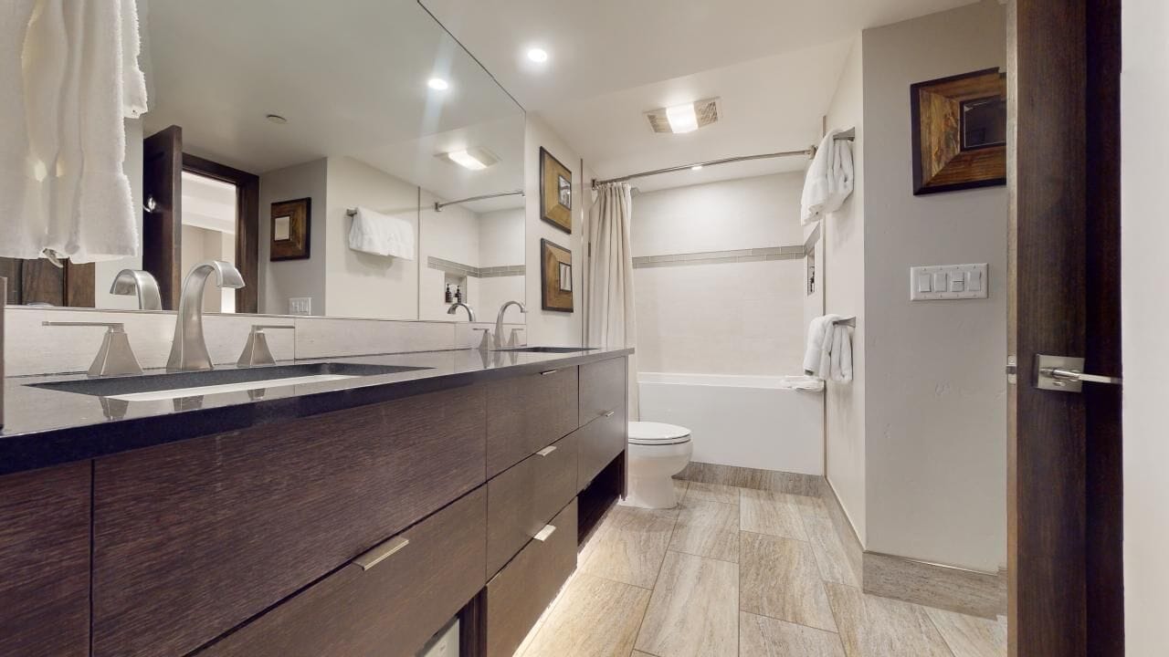 A modern bathroom with a large mirror, dark wood vanity, and a shower area.