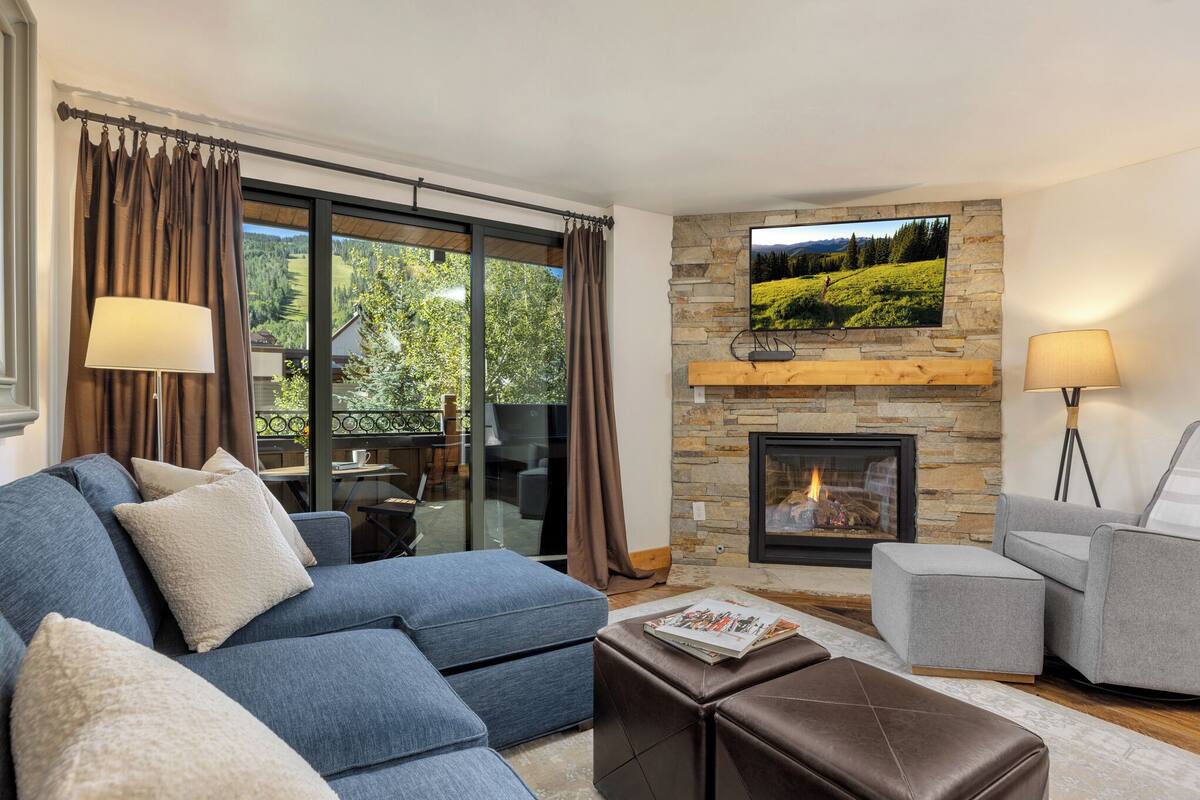 A modern living room with a sectional sofa, a fireplace, and a large window with curtains.