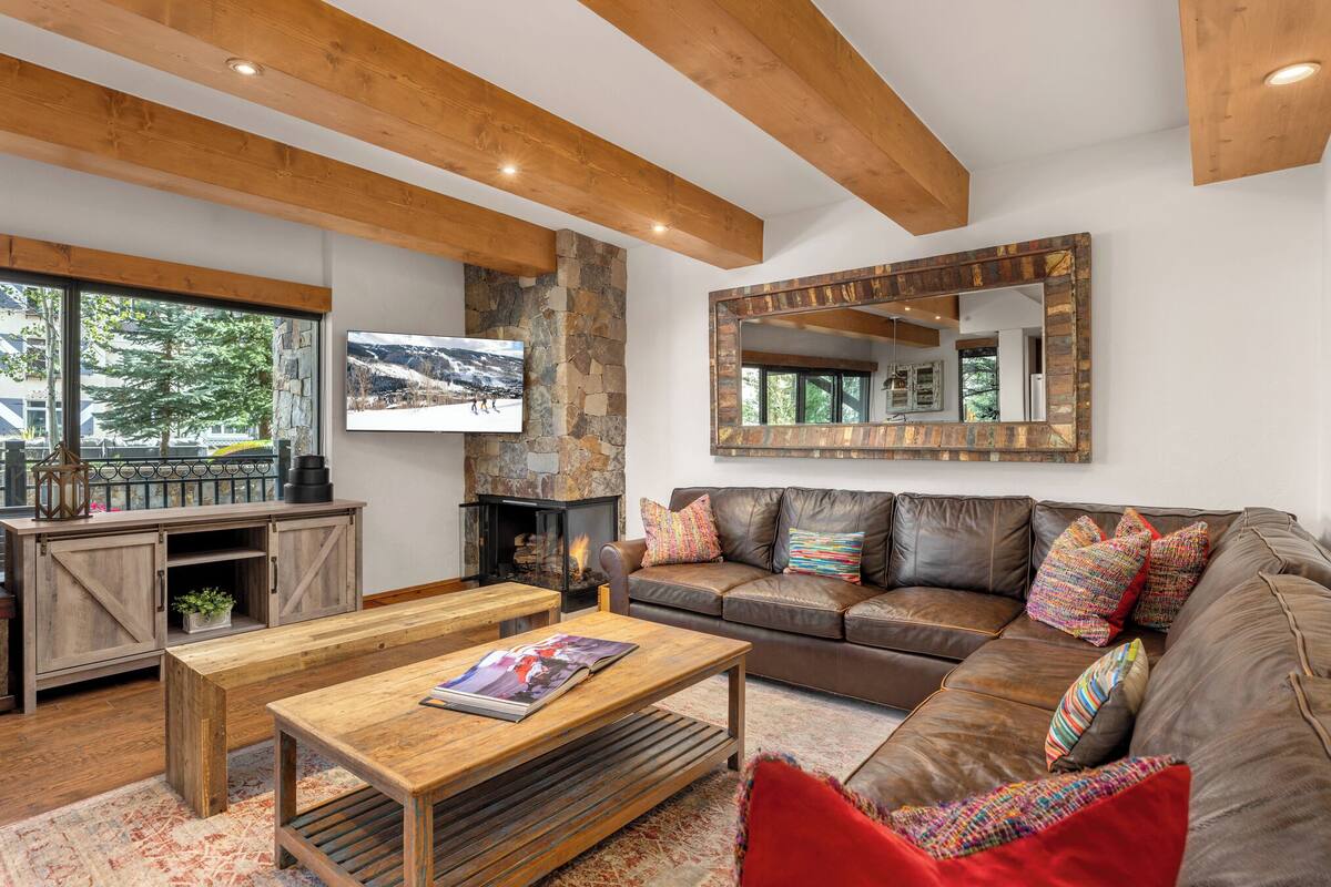 A cozy living room with a stone fireplace, a large mirror, and a leather sofa with colorful cushions.
