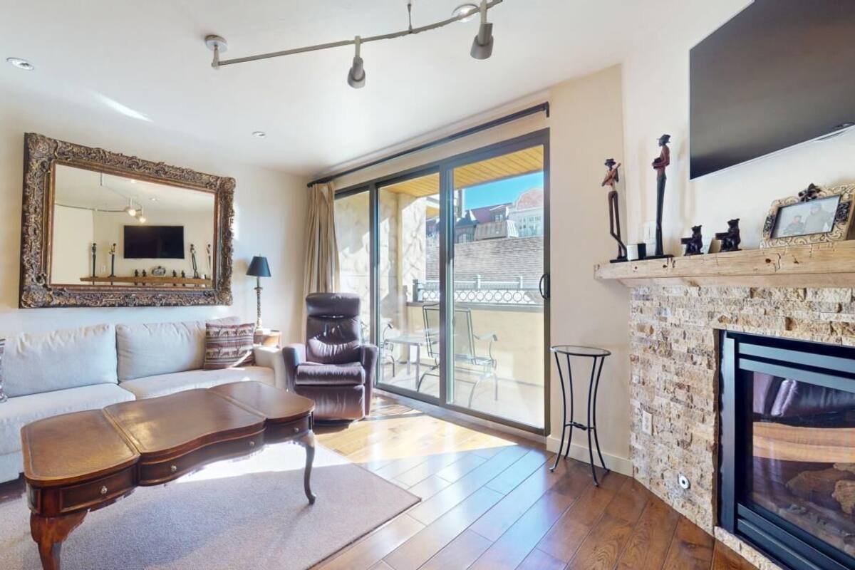 A spacious living room with a large mirror, a fireplace, a sofa, a leather armchair, and a dining area with a view of the outside.